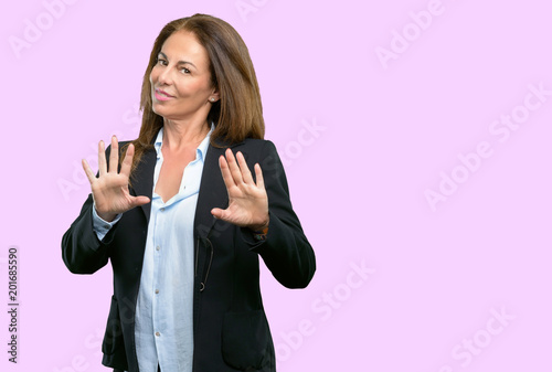 Middle age business woman annoyed with bad attitude making stop sign with hand, saying no, expressing security, defense or restriction, maybe pushing