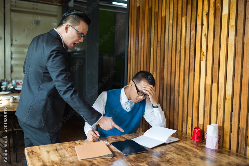 Manager shouted to the employee and point his finger to report, he is very angry for performance errors. employee is stressed and put hands on his head. Manager shouted to the employee and point his finger to report, he is very angry for performance errors. employee is stressed and put hands on his head.