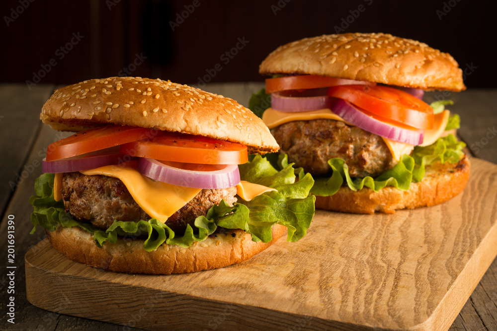 Home made hamburger with beef, onion, tomato, lettuce and cheese. Fresh burger close up on wooden rustic table with potato fries, beer and chips. Cheeseburger. Home made hamburger with beef, onion, tomato, lettuce and cheese. Fresh burger close up on wooden rustic table with potato fries, beer and chips. Cheeseburger.