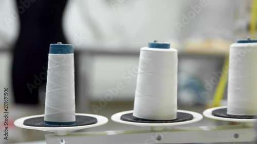 Closeup of three big bobbins with thin white thread on working professional sewing machine. Real time full hd video footage photo