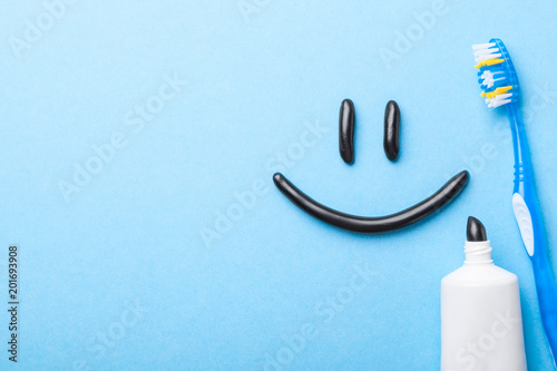 Black toothpaste from charcoal for white teeth. Toothpaste in the form of  smile on the face,  tube and  toothbrush on  blue background. Copy space for text