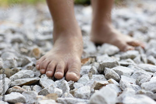 Fotografie Closeup of a girl bare feet walking on stones rock