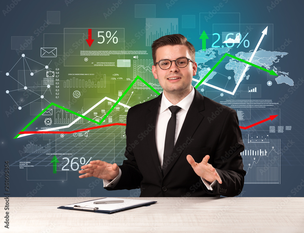 Young handsome businessman sitting at a desk with stocks and progress charts behind him Young handsome businessman sitting at a desk with stocks and progress charts behind him