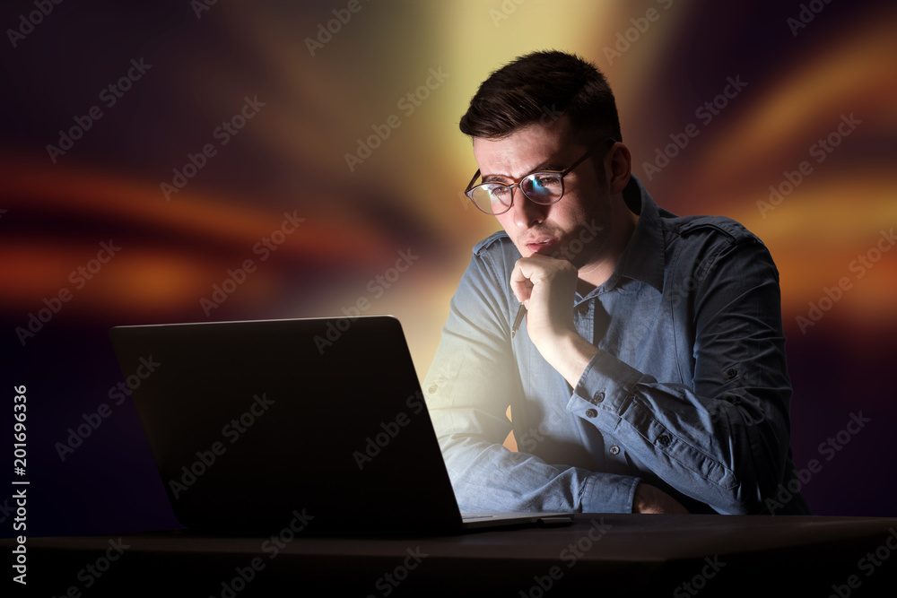 Young handsome businessman working late at night in the office with warm lights in the background Young handsome businessman working late at night in the office with warm lights in the background