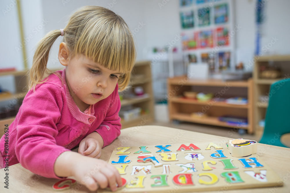 Fototapeta premium Little caucasian girl playing with wooden puzzle and space for text
