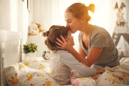 mother wakes her daughter in bed in  morning photo