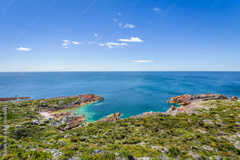 Stunning view from bright white light station to deep blue sea ocean bay turquoise water with orange red rocks at shore coast on warm sunny clear sky day, Rocky Cape National Park, Tasmania, Australia