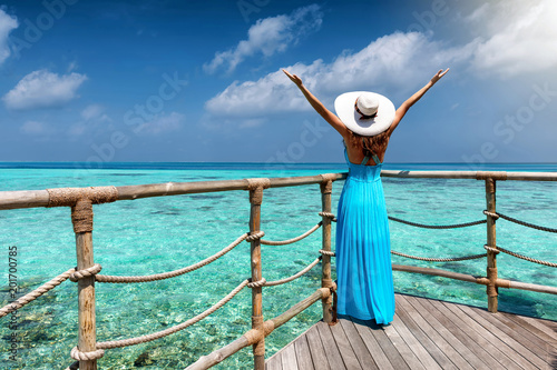 Glückliche Frau im blauen Kleid genießt die Aussicht auf das türkisfarbende Meer der Tropen photo