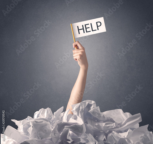 Female hand emerging from crumpled paper pile holding help sign 