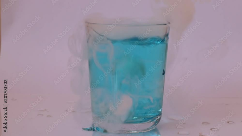 The blue water in glass and put dry ice inside and engender white smoke on white background. The blue water in glass and put dry ice inside and engender white smoke on white background.