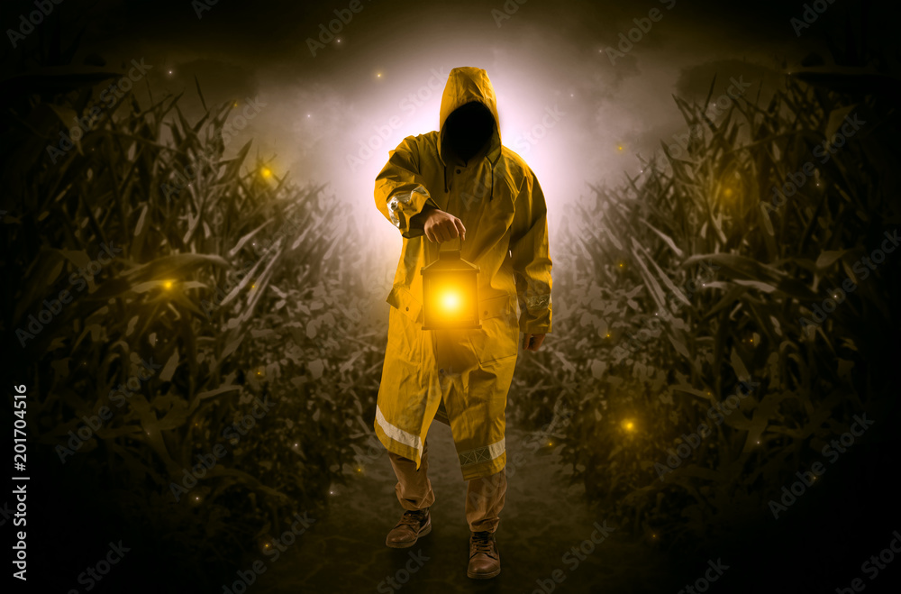 Fototapeta premium Man in raincoat at night coming from thicket and looking something with glowing lantern 