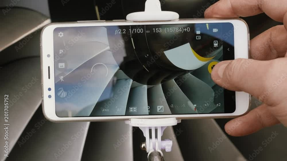 A man engineer photographs a jet engine. The man's hand takes a picture of the engine of the aircraft, using a modern smartphone and a monopod for selfie.