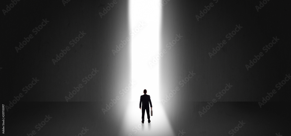 Businessman standing and seeing the light at the end of a big wall
