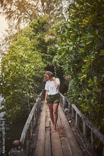 Traveling girl on the wooden bridge. Pretty young woman in the jungle. Summer lifestyle and adventure photo
