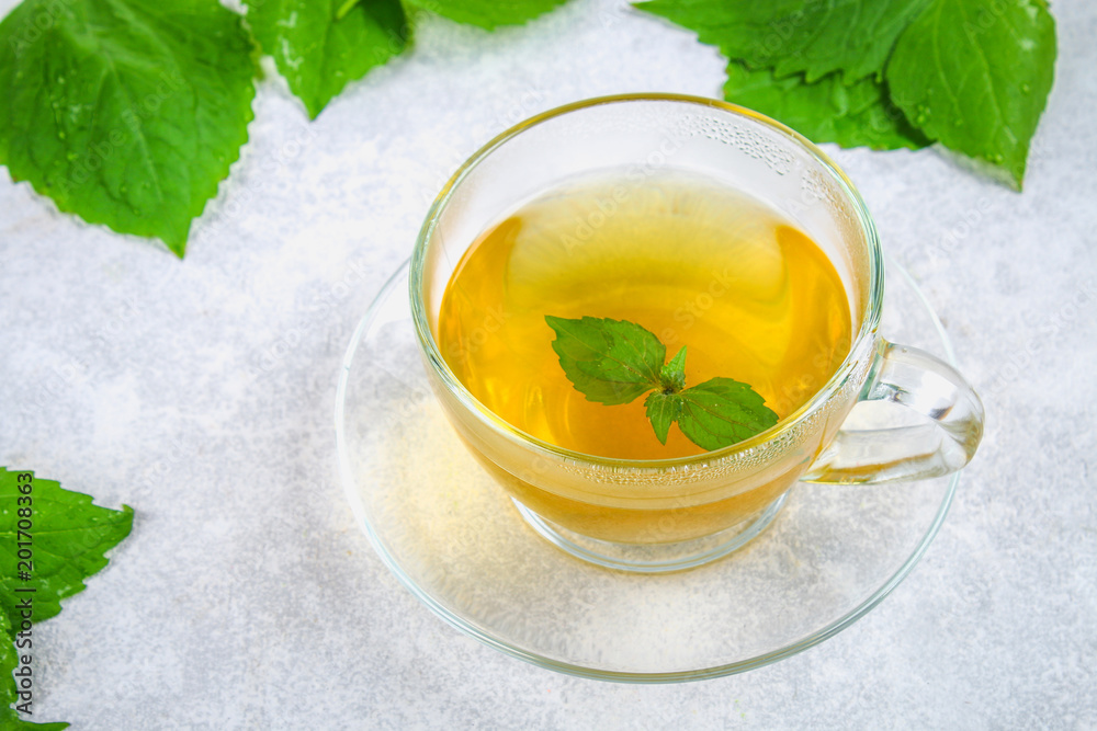 Leaves of fresh green nettle and a clear glass cup of herbal nettle tea on a gray concrete table. Leaves of fresh green nettle and a clear glass cup of herbal nettle tea on a gray concrete table.