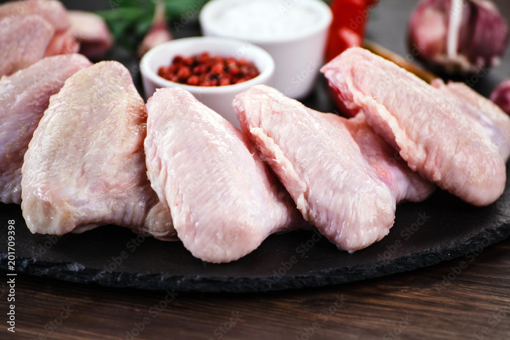 Raw chicken wings on black stone on wooden background Raw chicken wings on black stone on wooden background