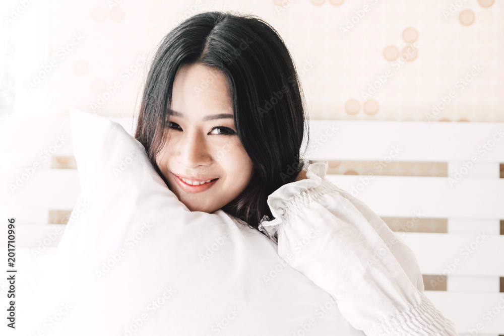 Beautiful woman smiling to camera and relaxing with pillow on the bed in her room at home Beautiful woman smiling to camera and relaxing with pillow on the bed in her room at home