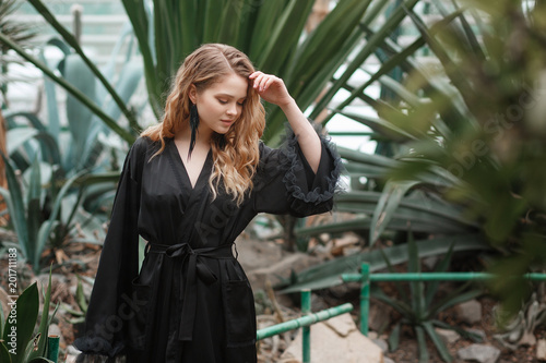 adorable young lady standing in the greenhouse among cactuses and succulents wearing black sleepwear