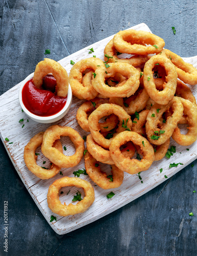 Fried Onion Rings with Ketchup on white cutting board.