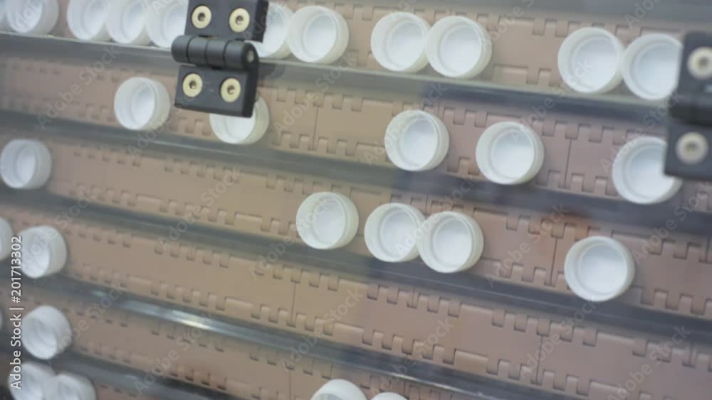 Conveyor supplying white plastic caps for bottles Conveyor supplying white plastic caps for bottles