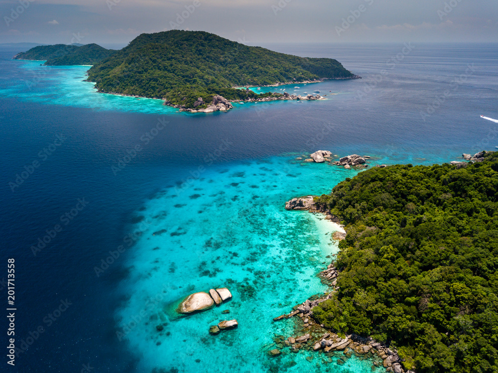 Aerial view of a deserted, jungle covered tropical island with crystal clear ocean below - obrazy, fototapety, plakaty 