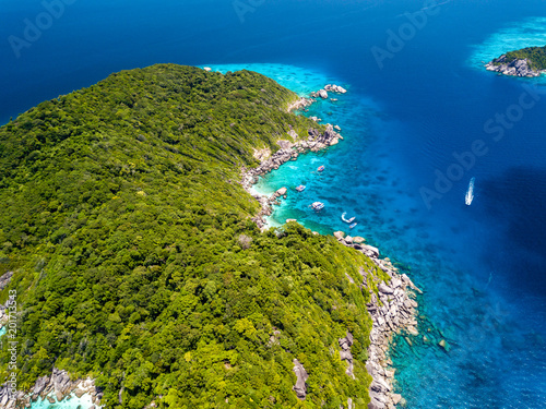 Fototapeta Naklejka Na Ścianę i Meble -  Aerial drone view of a boat over a coral reef next to a beautiful, empty, tree covered island