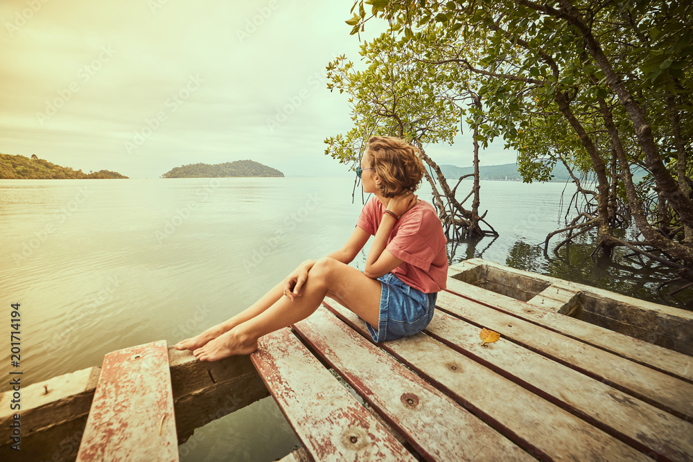 Traveling girl on the wood pier. Pretty young woman and tropical landscape. Summer lifestyle and adventure photo. Fish eye lens image
