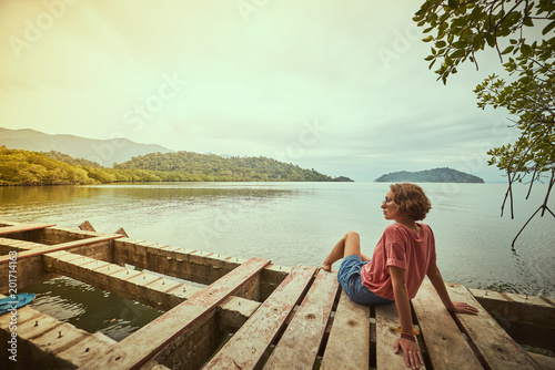 Traveling girl on the wood pier. Pretty young woman and tropical landscape. Summer lifestyle and adventure photo. Fish eye lens image