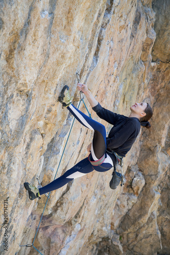 Woman climbs an overhang rock with a rope, lead