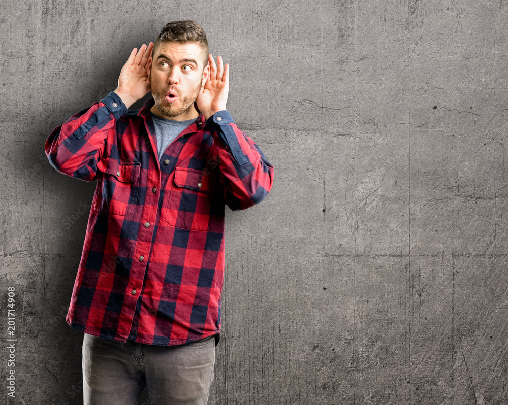 Young handsome man holding hand near ear trying to listen to interesting news expressing communication concept and gossip Young handsome man holding hand near ear trying to listen to interesting news expressing communication concept and gossip