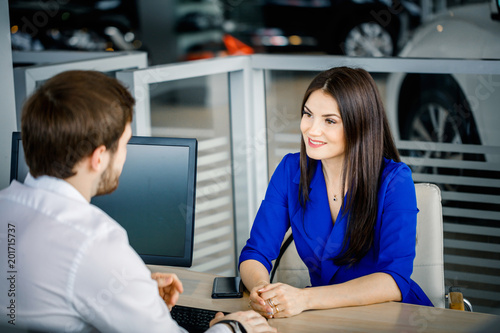 Sales rep talking to a happy female client trying to convince , new luxury car on background