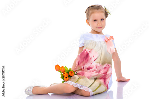 Little girl with bouquet of flowers sits on the floor.