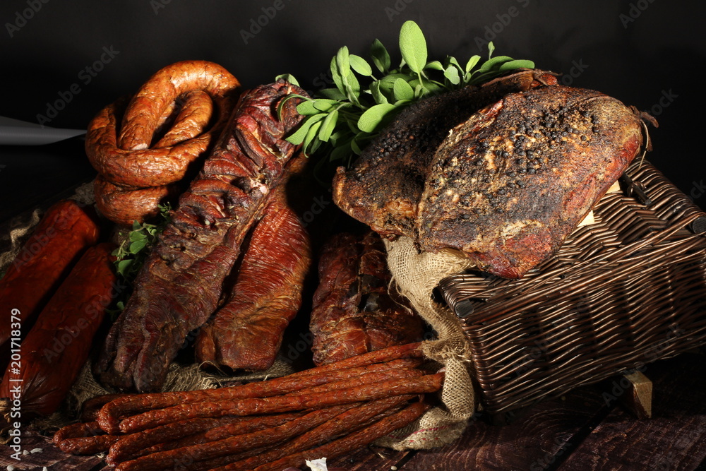 Fototapeta premium Kompozycja wędlin. Tradycyjnie wędzone wędliny w kompozycji na lnianym obrusie z ziołami