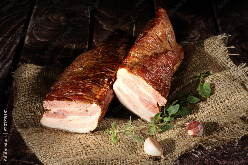 Fototapeta premium Boczek wędzony dymem olchowym. Tradycyjnie wędzone wędliny w kompozycji na lnianym obrusie z ziołami