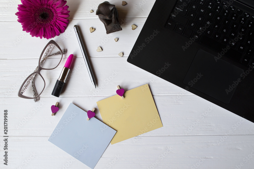 Laptop, colorful memo sheets, eyeglasses, stylus, pink gerbera and elements of decoration on a white wooden work desk. Beautiful female workplace top view. Laptop, colorful memo sheets, eyeglasses, stylus, pink gerbera and elements of decoration on a white wooden work desk. Beautiful female workplace top view.