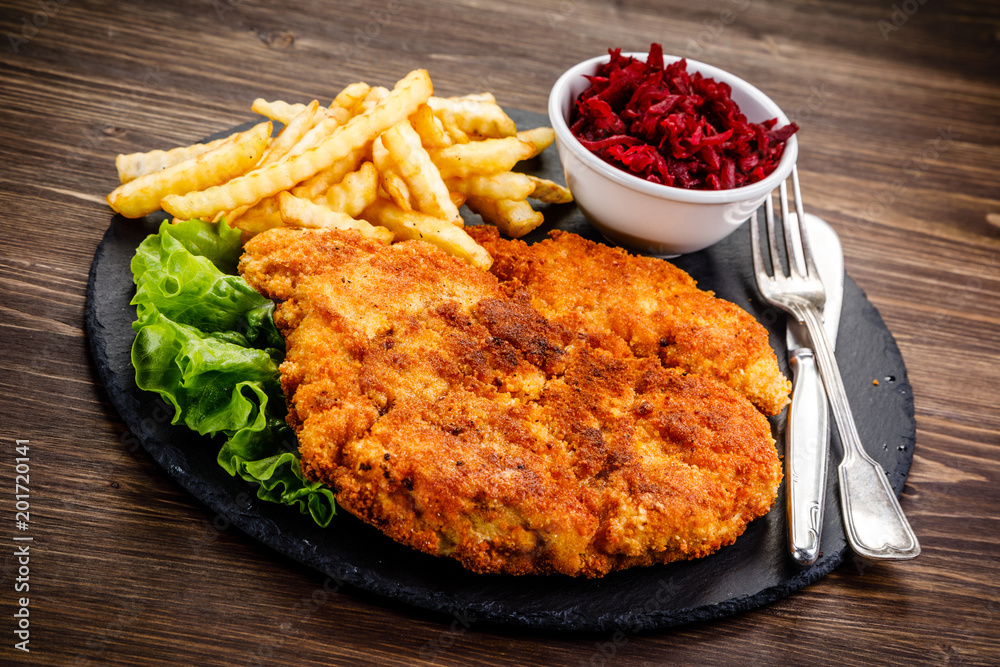 Fried pork chop, French fries and vegetables on wooden background Fried pork chop, French fries and vegetables on wooden background