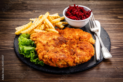 Fried pork chop, French fries and vegetables on wooden background