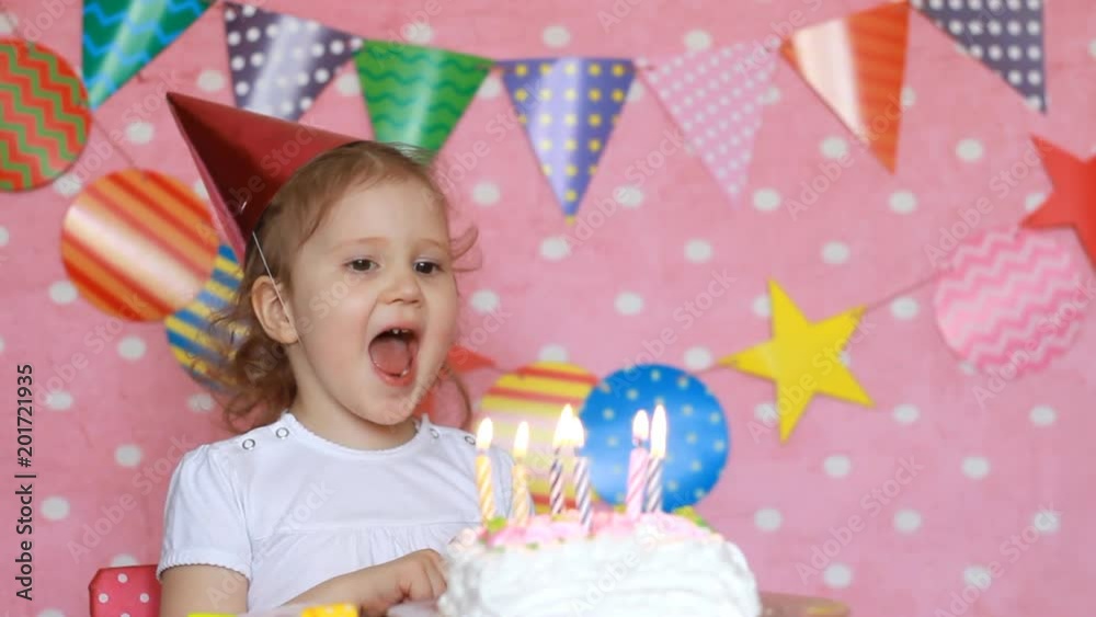 Decor Birthday and Ornament. Cute little girl and cake with candles. Happy child on the children's holiday. Pink background and colorful flags Decor Birthday and Ornament. Cute little girl and cake with candles. Happy child on the children's holiday. Pink background and colorful flags