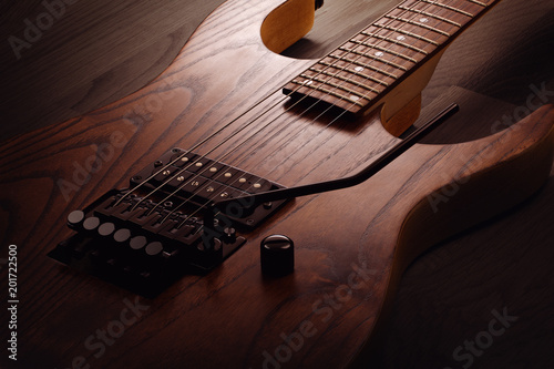 Close up on the body of custom electric guitar with natural finish, selective light on it, wooden background photo
