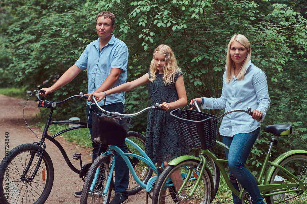 Fototapeta premium Attractive family dressed in casual clothes on a bicycle ride with their cute little spitz dog.