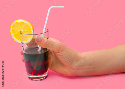 Hand girl holding fresh Juice glass with a straw slice of yellow lemon on a pink background. Fashion pastel summer design style concept