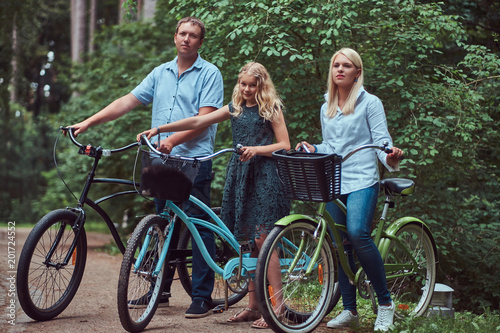 Attractive family dressed in casual clothes on a bicycle ride with their cute little spitz dog.