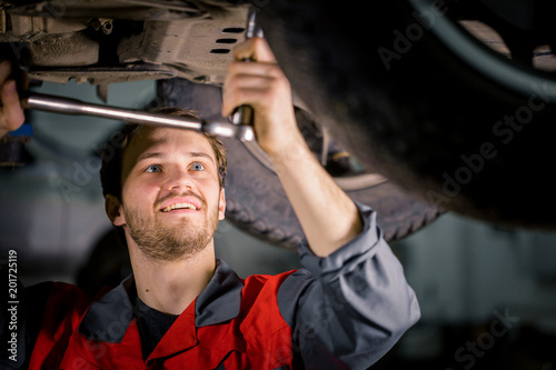 Quadro su tela Auto mechanic working at auto repair shop under car with tool