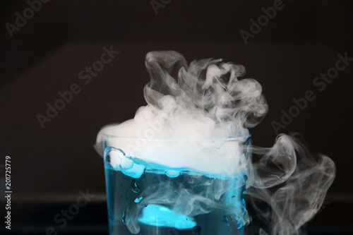 Dry ice in a glass of blue water and engender white smoke on black background.