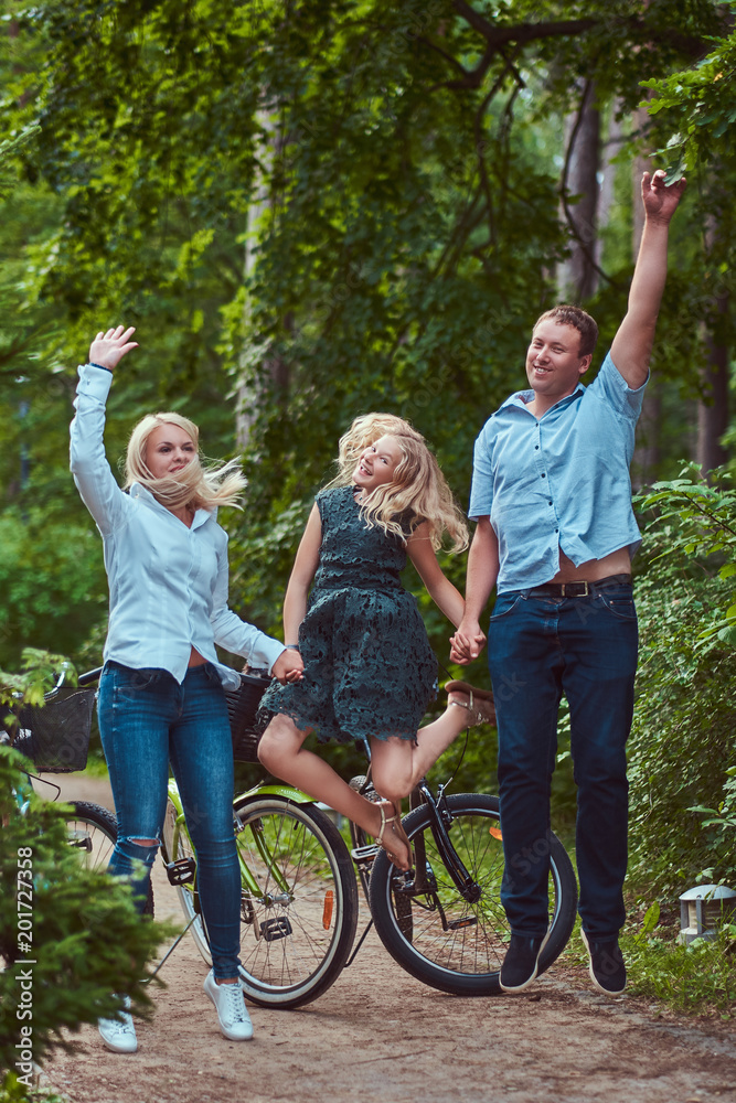 An attractive family dressed in casual clothes on a bicycle ride, have fun and jumping in a park. An attractive family dressed in casual clothes on a bicycle ride, have fun and jumping in a park.