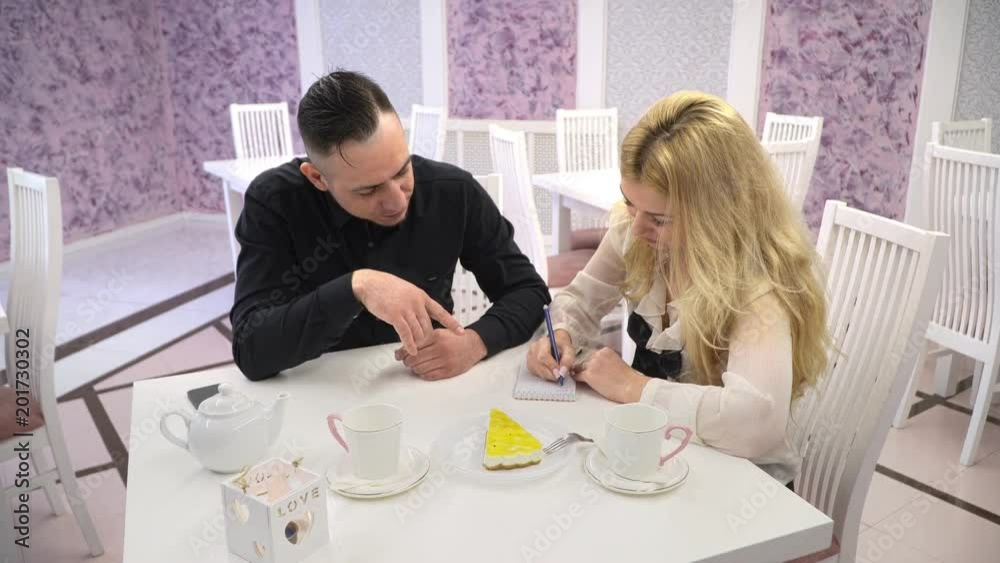 Loving couple in a cafe. Couple man and woman talking in the cute cafes and write in a notebook entry Loving couple in a cafe. Couple man and woman talking in the cute cafes and write in a notebook entry