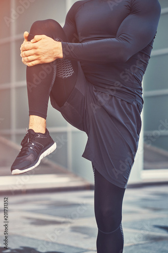 Young fitness man in a sportswear, doing stretching in the modern city against a skyscraper.