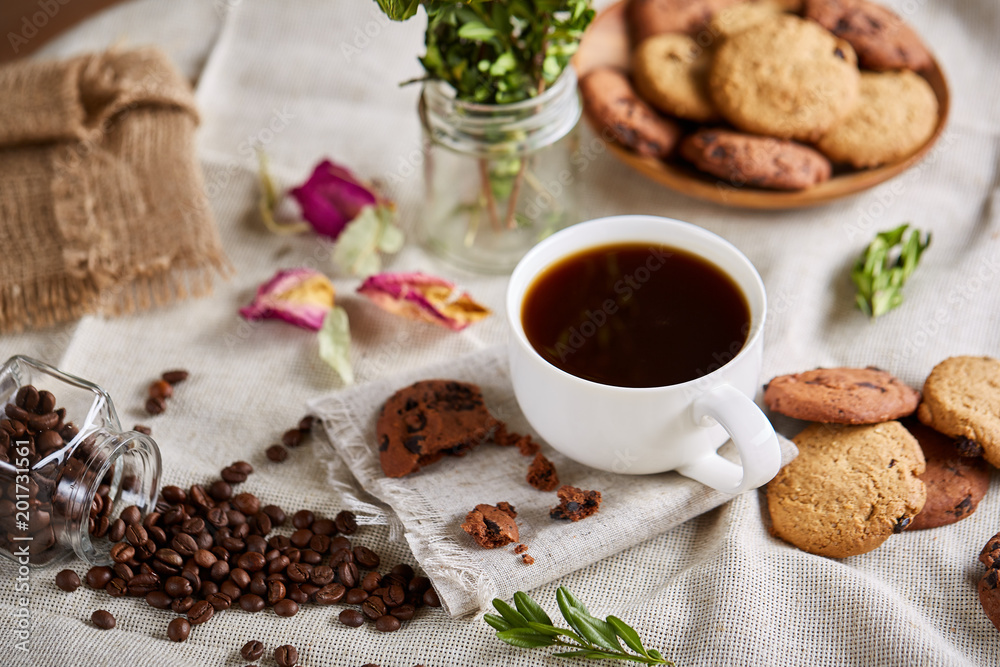 Morning coffee in white cup, chocolate chips cookies on cutting board close-up, selective focus