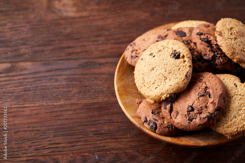 Side view of chocolate chip cookies on a wooden plate over rustic background, selective focus