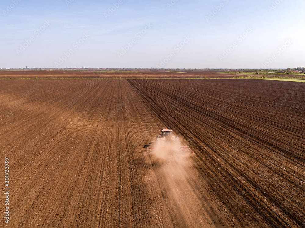 Obraz premium Aerial shot of a tractor cultivating field at spring